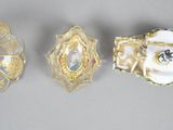 three pieces of glass with gold and white designs are on a gray surface