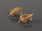a pair of gold leaf earrings on a reflective surface