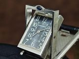 a small silver clock sitting on top of a black glove