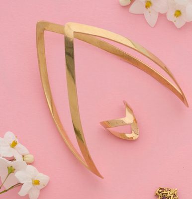 une broche en or et une paire de boucles d'oreilles posées sur un fond rose