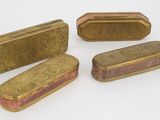 quatre petites boîtes en laiton sont alignées sur une surface blanche