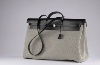 a grey and black bag with a black handle on a white surface