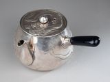 a silver tea pot with a black handle on a white table