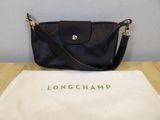 un sac à main Longchamp noir posé sur un sac blanc