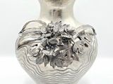 a silver vase with flowers on it sitting on a table