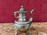 silver plated teapot on marble table with red wall in background