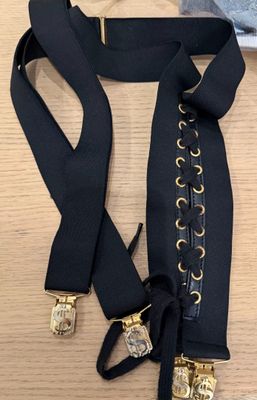 une ceinture noire ornée de boucles dorées posée sur une table en bois