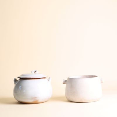 un pot à crème et un sucrier posés sur une surface blanche, sur fond beige