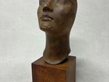 une image représentant une sculpture en bronze représentant une tête, posée sur un socle en bois