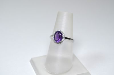 une image représentant une bague ornée d'une pierre violette posée sur un socle blanc