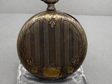 a gold colored pocket watch on a clear stand