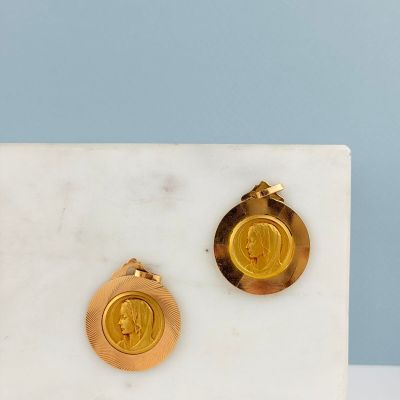 un gros plan sur une paire de boucles d'oreilles en or posées sur une surface en marbre