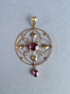 a close up of a gold pendant with a red stone on it