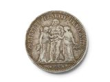 une vieille pièce d'argent posée sur une surface blanche, sur laquelle figure l'image d'un groupe de personnes