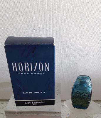 un vase en verre bleu posé sur une table à côté d'un coffret de parfum « Horizon »