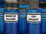 several blue bottles with labels are lined up on a shelf
