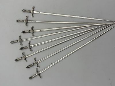six pairs of silver - plated swords are displayed on a table