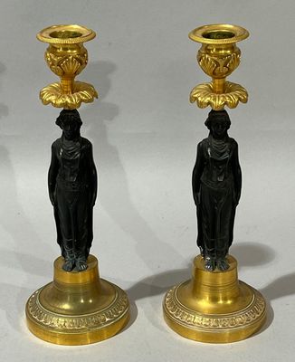 deux bougeoirs noirs et dorés posés l'un à côté de l'autre sur une surface blanche
