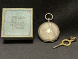 a close up of a pocket watch and a key on a table
