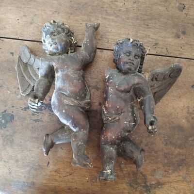 paire d'ustensiles anciens en fonte représentant des anges, posés sur une table en bois