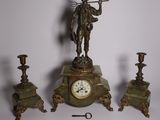 a clock with a statue on top of it next to three candles