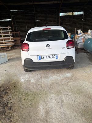 une voiture blanche garée dans un garage, à côté d'une pile de bagages