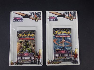 Deux paquets de cartes à collectionner Pokémon sont posés sur une surface noire.