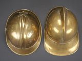 pair of antique brass fire helmets on a black background