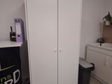 a white cabinet in the corner of a room with a black trash can