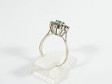 an image of a diamond and emerald ring on a clear stand