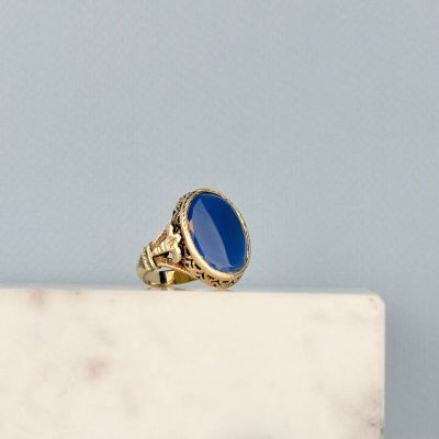 une image représentant une bague en or sertie d'une pierre bleue, posée sur un bloc de marbre