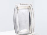 assiette rectangulaire en argent posée sur un socle blanc, avec un fond blanc