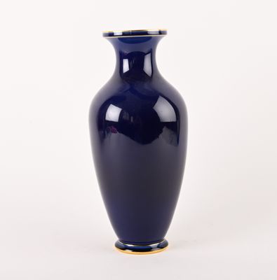 un vase bleu bordé d'or posé sur une surface blanche