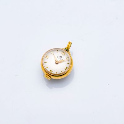 une petite montre de poche en or posée sur une surface blanche