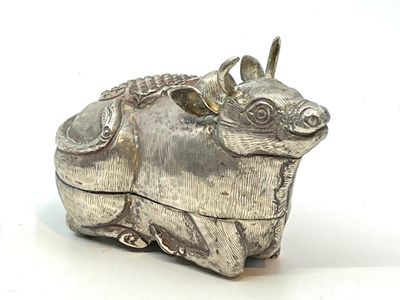 une figurine en argent représentant une vache, posée sur un fond blanc