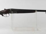 un fusil posé sur un socle transparent, devant un fond blanc