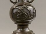 a bronze vase on a stand with a candle on top