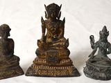 trois statues de Bouddha en bronze, assises sur un socle blanc