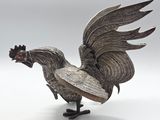 a silver statue of a rooster with a red eye