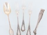 cinq cuillères en argent et une fourchette sont disposées sur une surface blanche