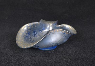 un objet en forme de coquillage, de couleur argentée et bleue, posé sur une surface noire