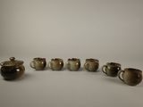 six cups and a teapot are lined up in a row