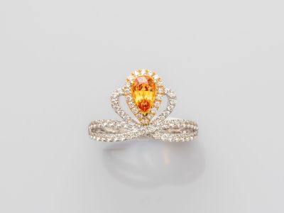 une bague sertie d'un saphir orange et de diamants, sur fond blanc