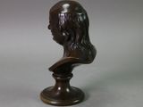 a bronze bust of a man with long hair on a pedestal