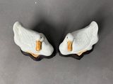pair of white ceramic ducks with orange beaks sitting on a gray surface