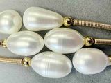 six perles blanches sont montées sur un bracelet plaqué or, sur un fond gris