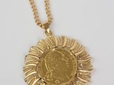 a close up of a gold necklace with a coin on it