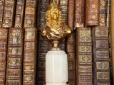 many old books on a shelf with a statue on top