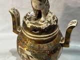 une théière en argent et or avec un chien sur le dessus