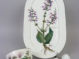 a white plate with purple flowers on it next to a cup and saucer